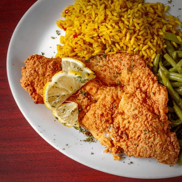 Crispy fried chicken with lemon slices, yellow rice, and green beans on a white plate.