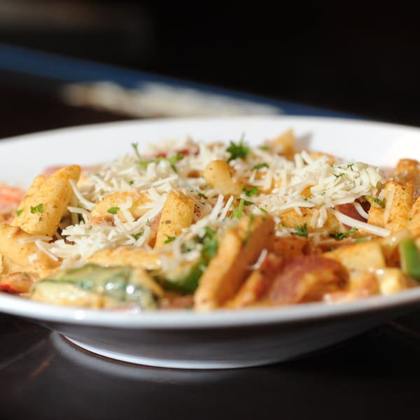 Close-up of Next Phaze Cafe's soul food pasta dish, topped with shredded cheese and herbs.