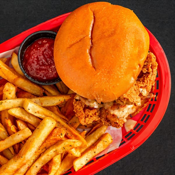 Next Phaze Cafe's fried chicken sandwich with melted cheese, fries, and ketchup in a red basket.