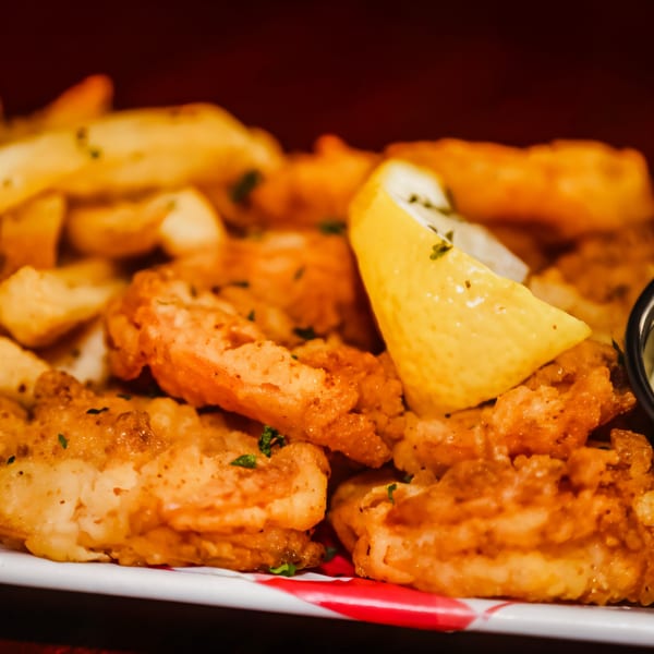 Golden-fried shrimp and french fries with a lemon wedge and parsley on a white plate.