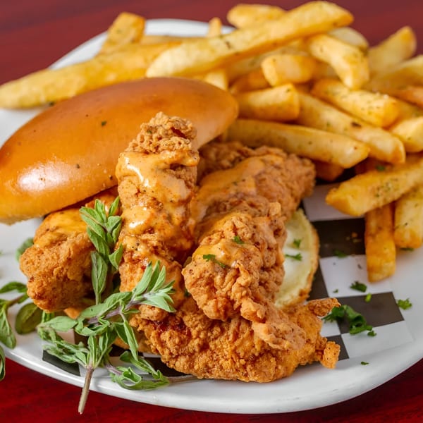 Crispy fried chicken tenders with sauce, a bun, and french fries on a white plate.