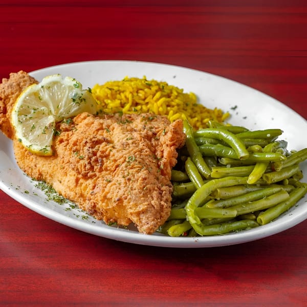 Next Phaze Cafe's fried fish with lemon, yellow rice, and green beans on a white plate.
