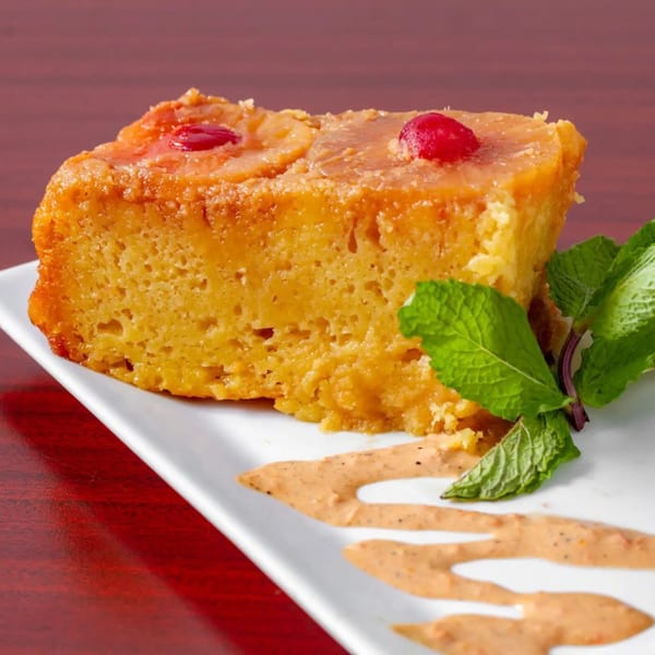 A slice of golden pineapple upside-down cake with cherries and mint on a white plate.