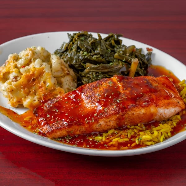 A soul food meal with salmon, mac and cheese, collard greens, and yellow rice on a white plate.