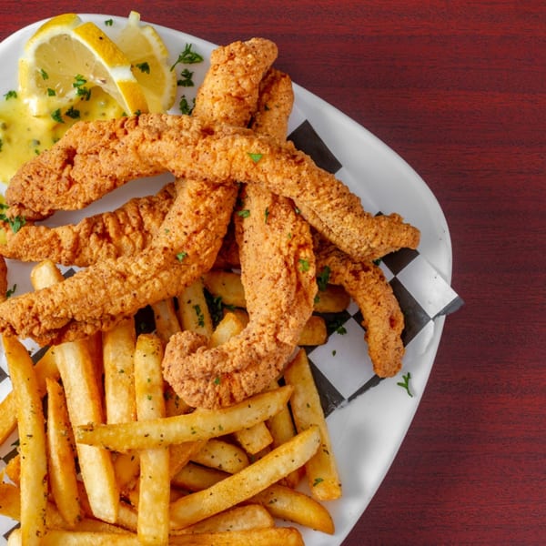 Crispy fried catfish strips and golden french fries with lemon wedges and a creamy sauce.
